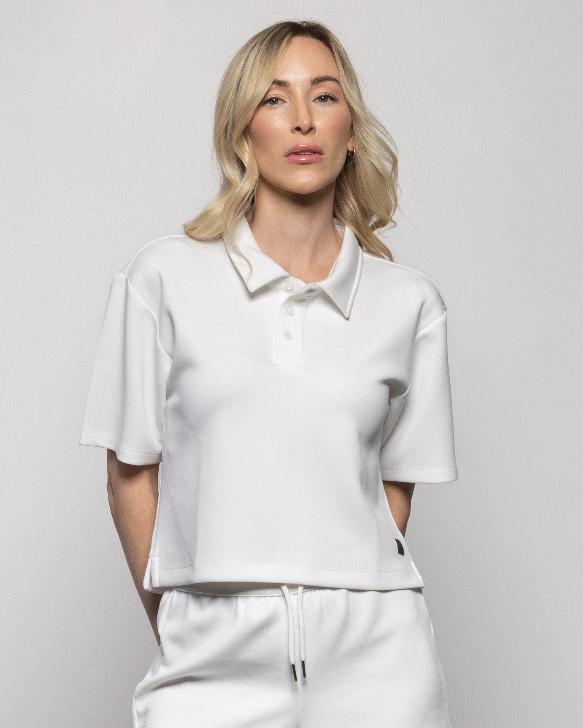 White polo shirt with short sleeves, button collar; paired with drawstring shorts