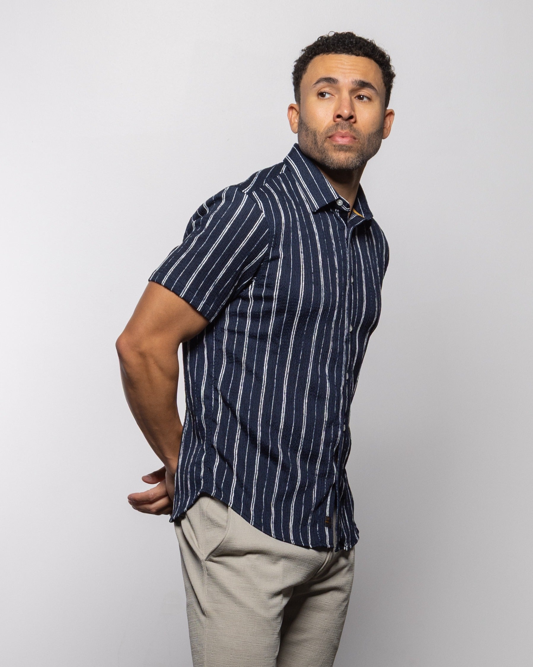 Men's short-sleeve indigo striped button-up shirt, side profile with curved hem