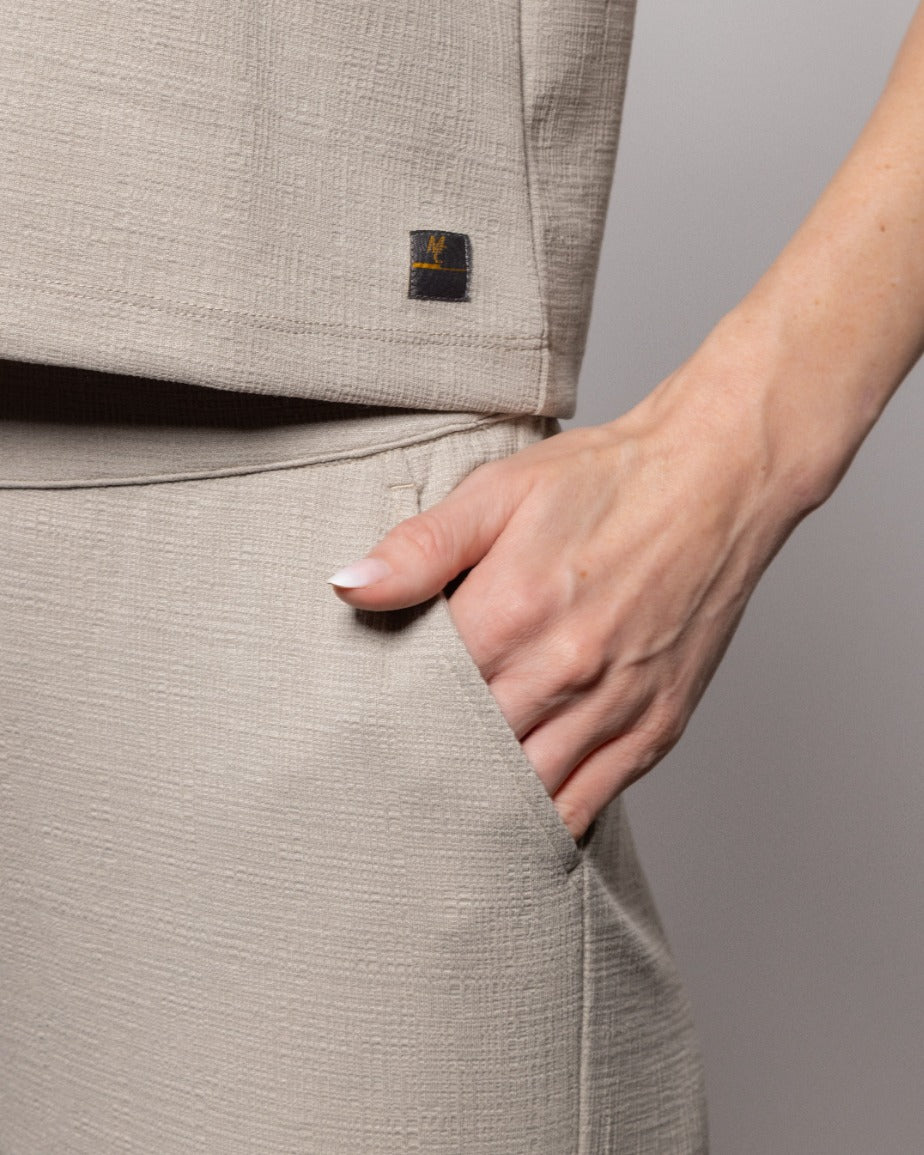 Beige textured crop pants detail: elastic waistband and stitched pocket edge.